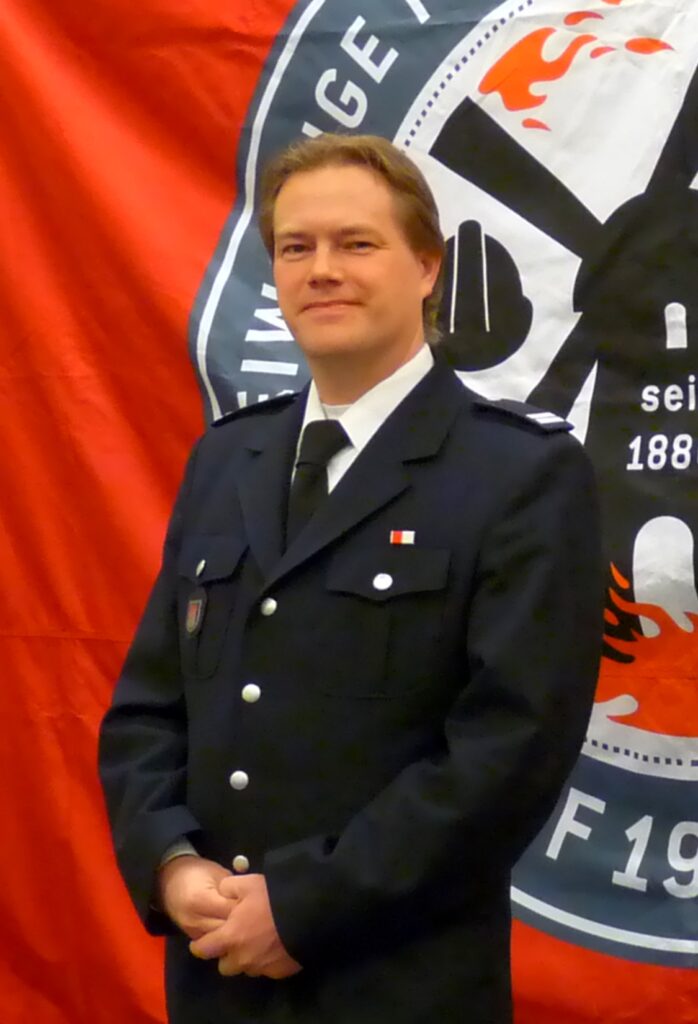 Mann in Feuerwehruniform vor rotem Banner