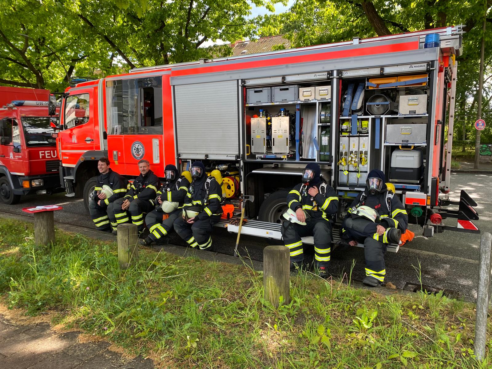 Feuerwehrleute sitzen vor Feuerwehrauto und rasten.