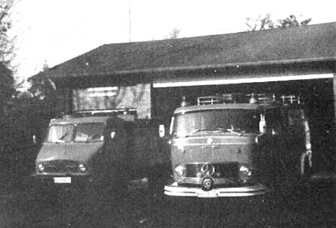 Zwei alte Feuerwehrfahrzeuge vor einer Garage.